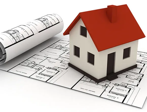 A toy house with a red roof sat on top of plans.